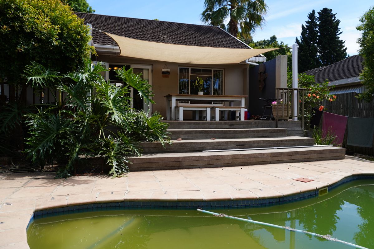 Rear exterior view featuring a swimming pool, raised timber deck, and a shade sail over the patio area.