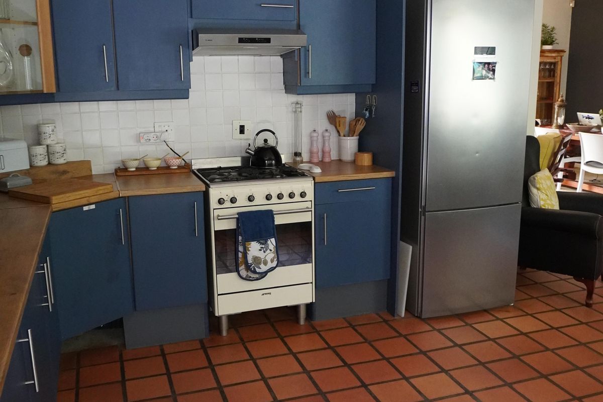A functional kitchen featuring blue cabinetry, a gas stove with extractor fan, tiled backsplash, and terracotta floor tiles.