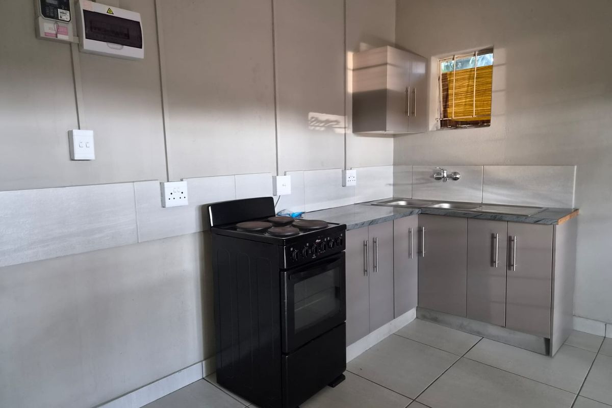 A functional kitchen featuring built-in cabinetry, a stainless steel sink, tiled splashback, and an electric stove with exposed electrical conduit.