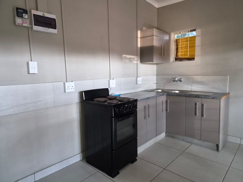 A functional kitchen featuring built-in cabinetry, a stainless steel sink, tiled splashback, and an electric stove with exposed electrical conduit.