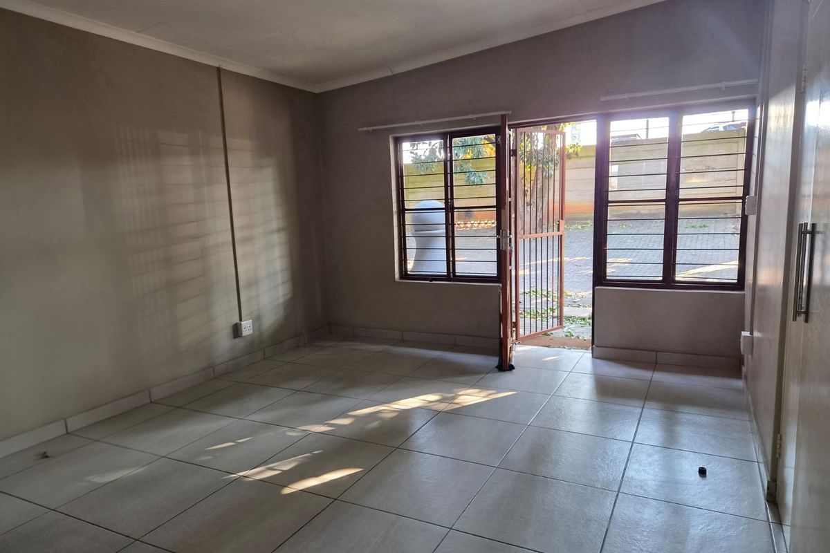 An empty living room featuring tiled flooring, security gates, and burglar bars, offering a blank canvas for personalization.