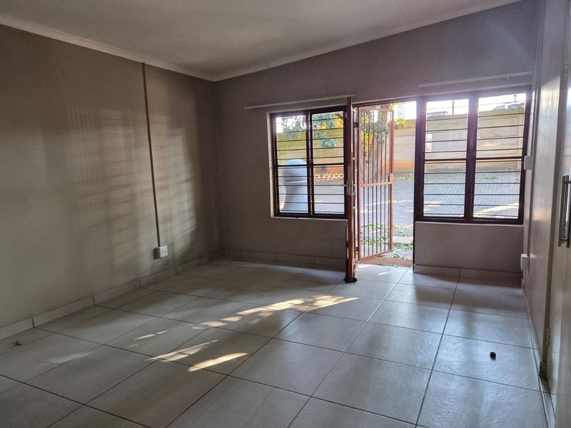 An empty living room featuring tiled flooring, security gates, and burglar bars, offering a blank canvas for personalization.