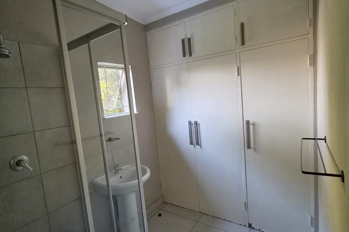 A functional bathroom featuring a shower enclosure, pedestal basin, and ample built-in storage cupboards with tiled flooring throughout.