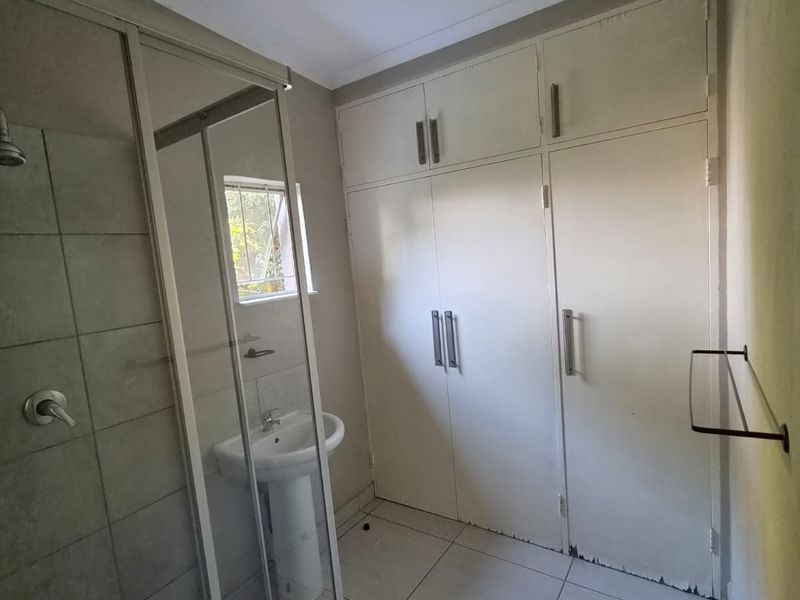 A functional bathroom featuring a shower enclosure, pedestal basin, and ample built-in storage cupboards with tiled flooring throughout.