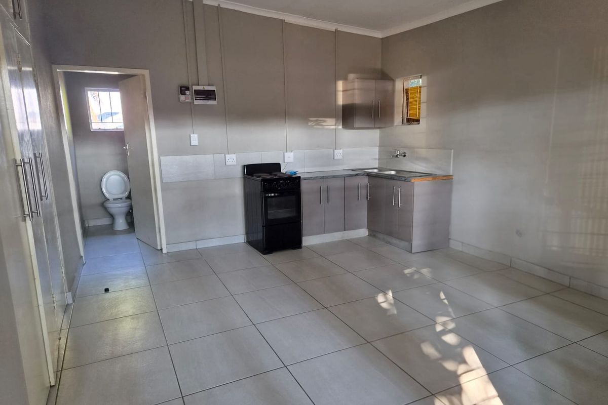 Open-plan kitchen area featuring tiled flooring, built-in cabinetry, and a freestanding stove, with an adjacent bathroom visible through the doorway.