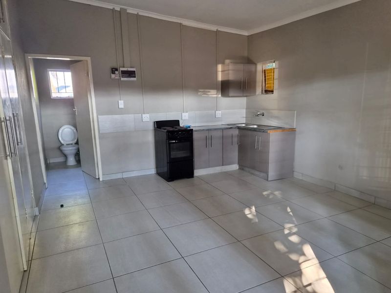 Open-plan kitchen area featuring tiled flooring, built-in cabinetry, and a freestanding stove, with an adjacent bathroom visible through the doorway.