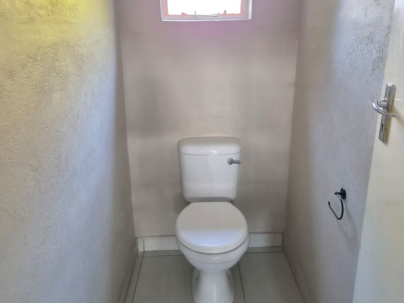 A compact, functional bathroom featuring tiled flooring, a standard toilet, and a small window with security bars.