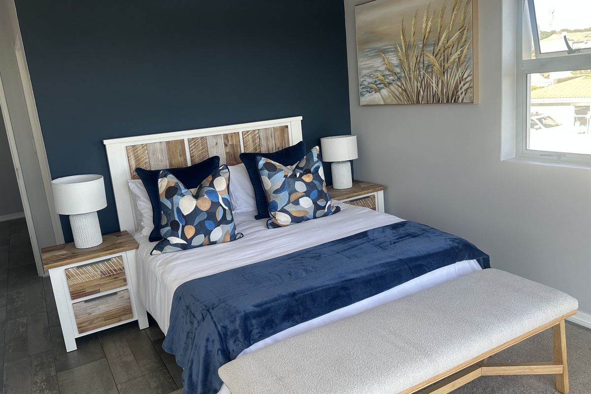 A well-maintained bedroom featuring a mix of tiled and carpeted flooring, a dark blue accent wall, and natural light from an aluminium-framed window.
