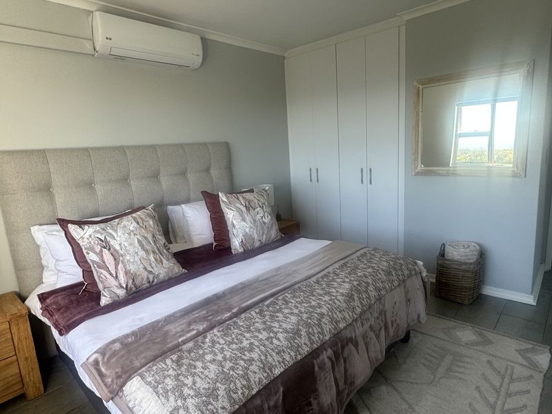A well-maintained bedroom featuring built-in cupboards, tiled flooring, and a wall-mounted split-system air conditioner for climate control.