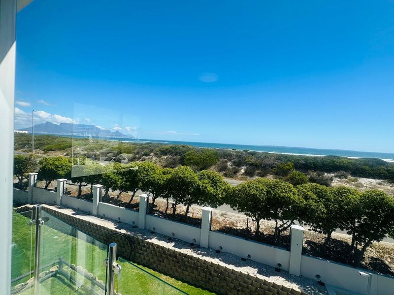 Elevated view overlooking the coastline, featuring a modern glass balustrade and a well-maintained boundary wall with landscaped greenery.
