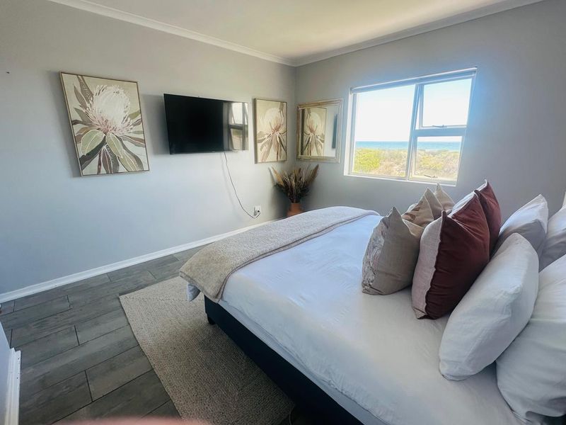 A well-maintained bedroom featuring tiled flooring, neutral wall finishes, and a window offering a pleasant coastal view.