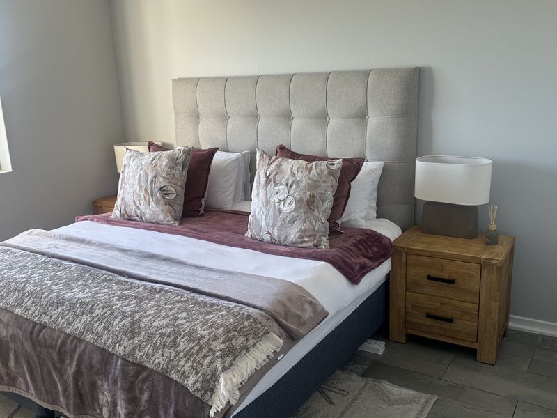 A well-maintained bedroom featuring neutral wall tones, tiled flooring, and a large window allowing for natural light.