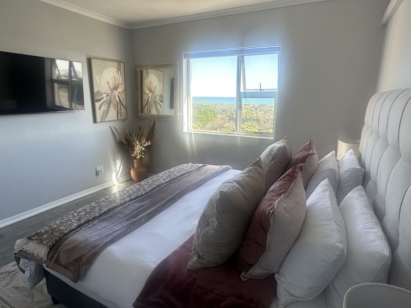 A well-maintained bedroom featuring tiled flooring, a coved ceiling, and a window offering a pleasant coastal view.