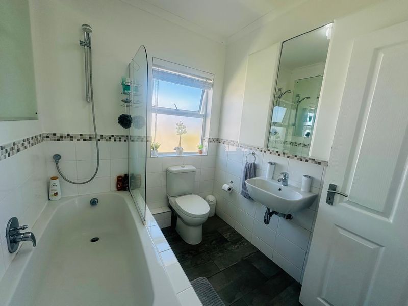 A functional bathroom featuring a bathtub with a shower mixer, glass screen, wall-mounted basin, and a medicine cabinet with tiled finishes.