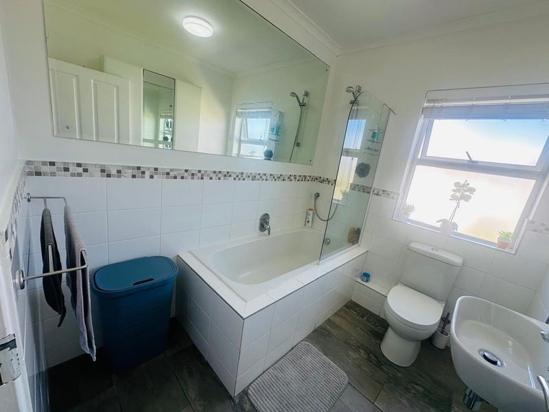 A functional bathroom featuring a built-in bathtub with a glass shower screen, a toilet, a bidet, and a large wall-mounted mirror.