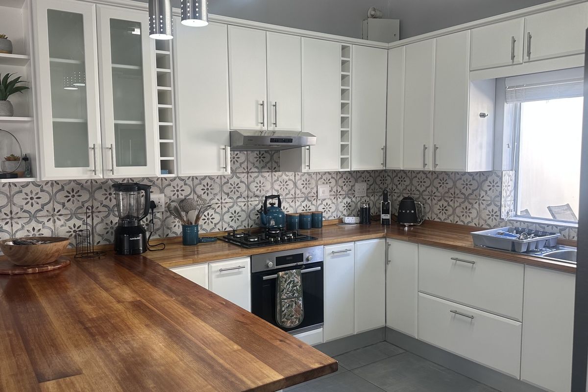 A well-maintained kitchen featuring white cabinetry, warm wooden countertops, a decorative patterned tile backsplash, and integrated appliances.