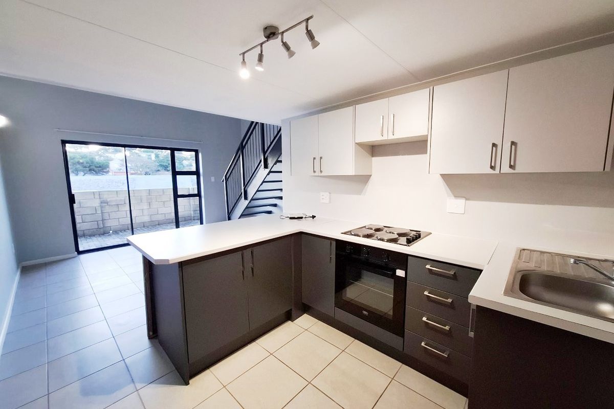 Modern open-plan kitchen featuring two-tone cabinetry, built-in oven and hob, tiled flooring, and direct access to an outdoor area via sliding glass doors.