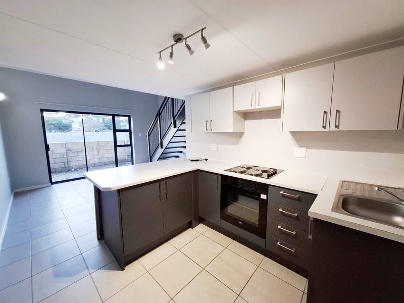 Modern open-plan kitchen featuring two-tone cabinetry, built-in oven and hob, tiled flooring, and direct access to an outdoor area via sliding glass doors.