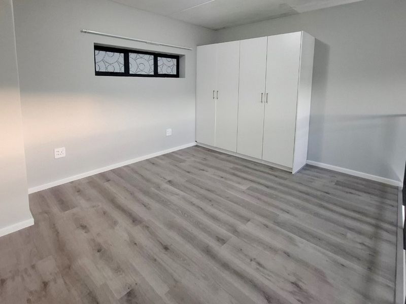 A clean, empty bedroom featuring modern laminate flooring, built-in white cupboards, and a horizontal window, overlooking a lower level via a metal balustrade.