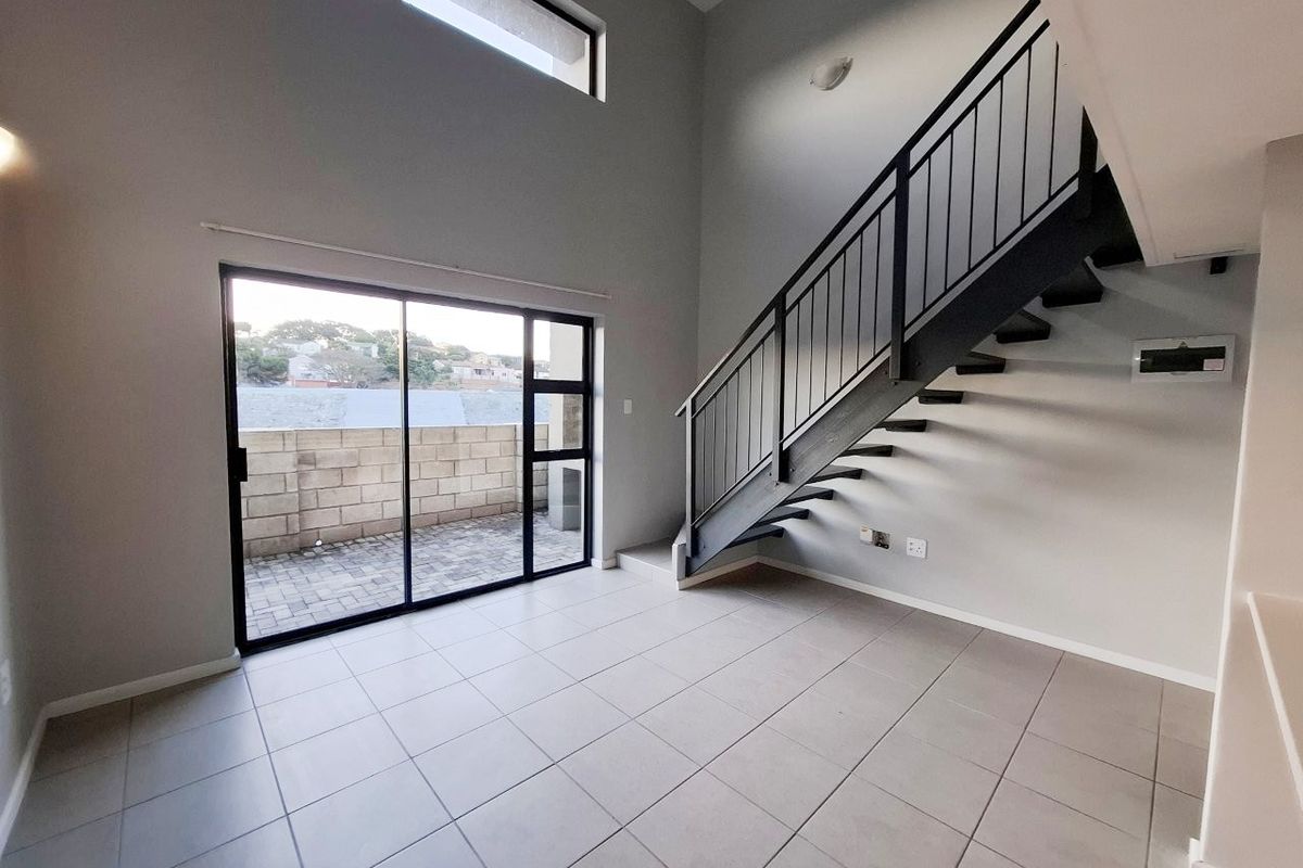 A bright, double-volume living area featuring modern tiled floors, a sleek metal staircase, and large sliding doors leading to an outdoor patio.