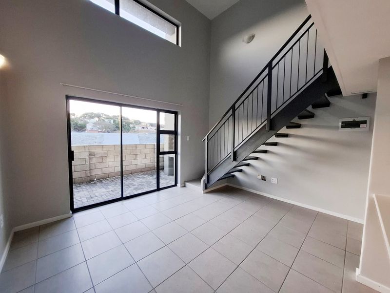 A bright, double-volume living area featuring modern tiled floors, a sleek metal staircase, and large sliding doors leading to an outdoor patio.