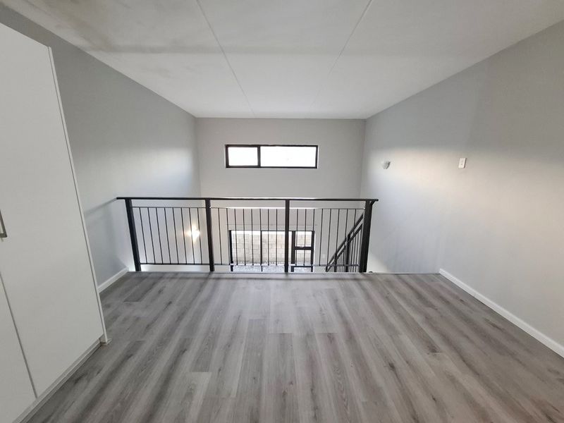 A bright, empty mezzanine bedroom featuring modern laminate flooring, a sleek metal balustrade, and a built-in wardrobe.