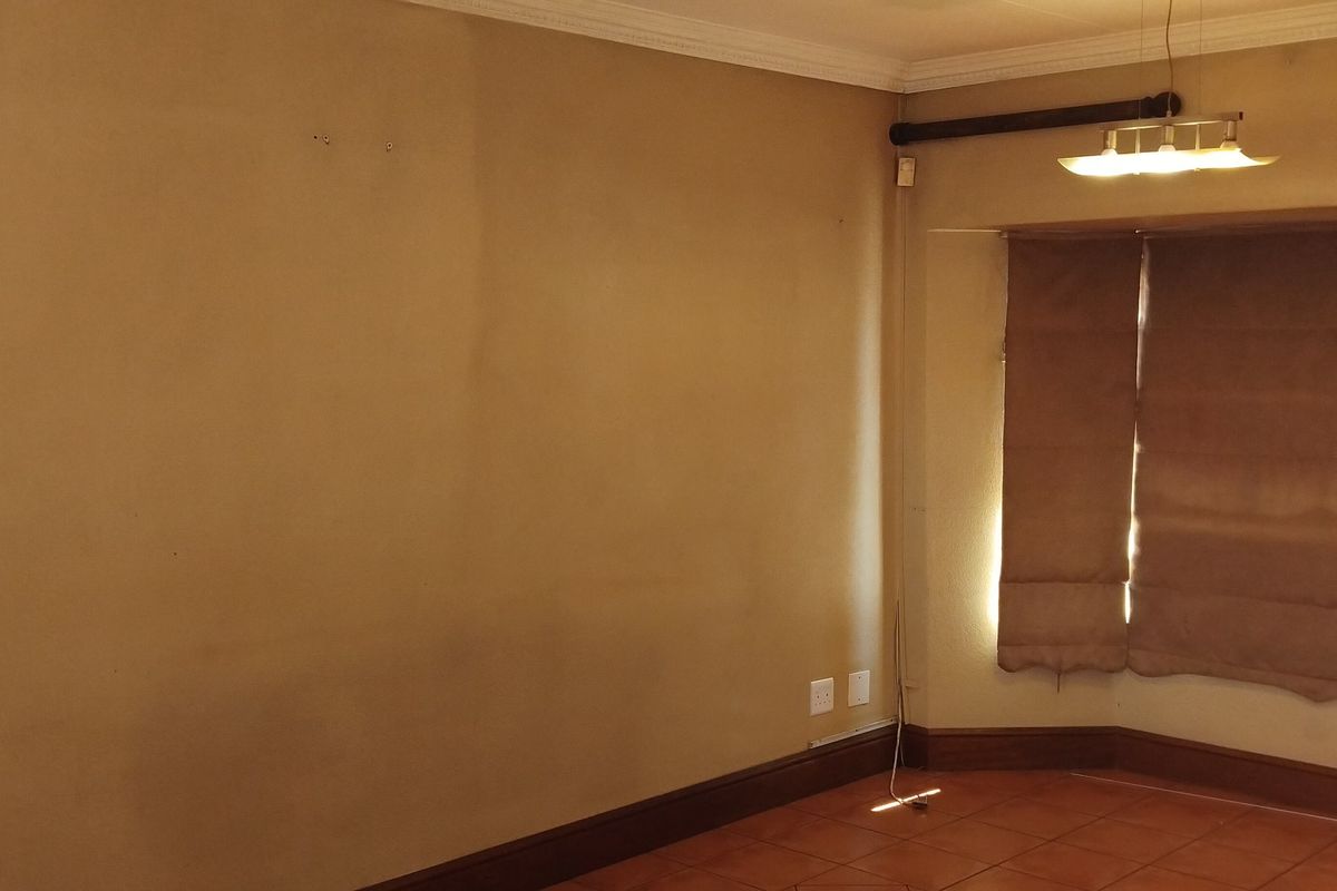 A living area featuring tiled flooring, crown molding, and a bay window with fitted blinds, providing a neutral foundation for interior design.
