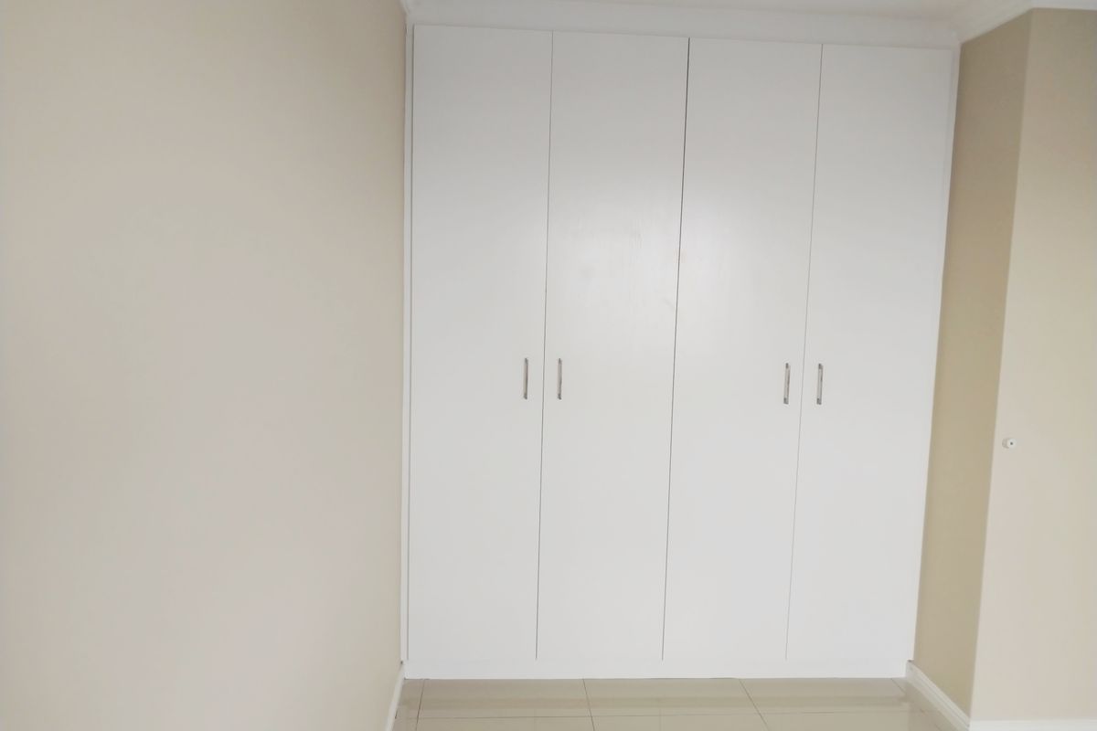 A clean, modern bedroom featuring built-in white cabinetry with sleek handles and neutral tiled flooring.