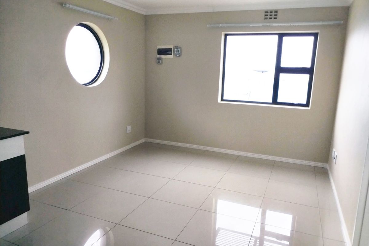 A bright, empty living area featuring polished porcelain floor tiles, a unique circular window, and a standard rectangular window with dark frames.
