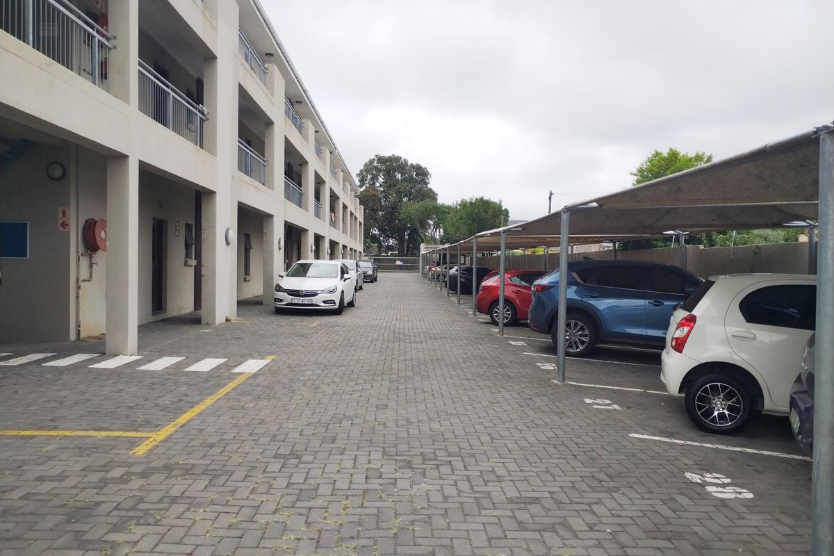 Exterior view of the apartment complex parking area featuring paved ground and covered parking bays for residents.