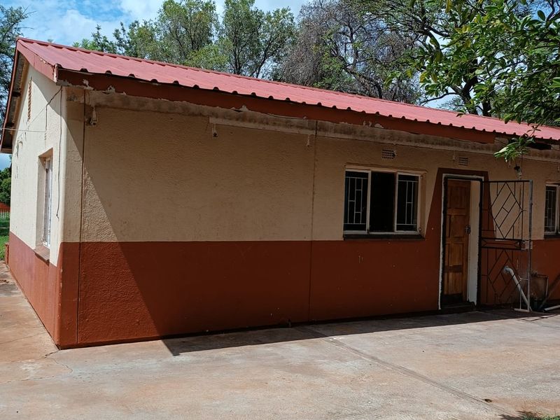 Rear view of a single-story house featuring a metal roof, security gates, and a concrete patio area in need of exterior maintenance.