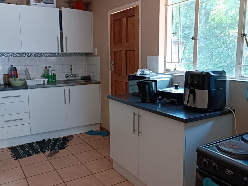 A functional kitchen featuring white cabinetry, tiled flooring, and a window with security bars. The ceiling shows signs of water damage requiring repair.