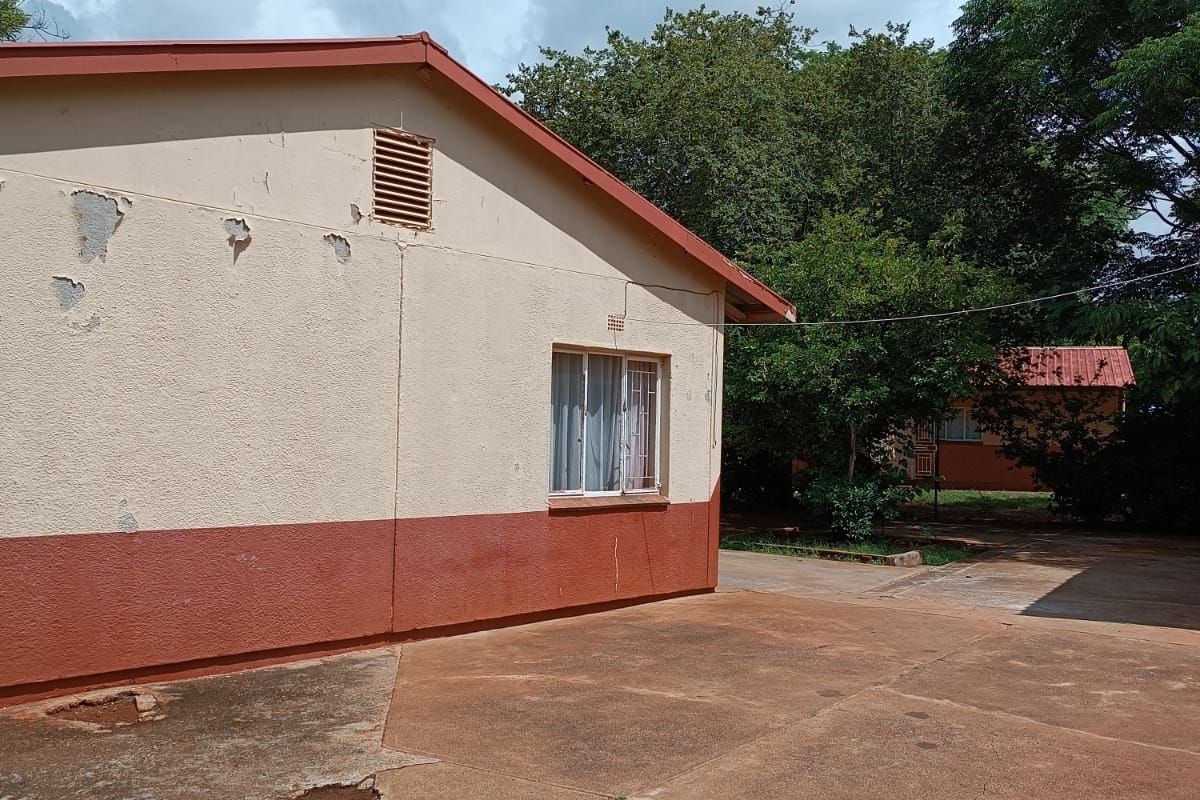 Rear exterior view of the property featuring a concrete driveway, gable roofline, and visible wear to the exterior wall paint and paving surfaces.