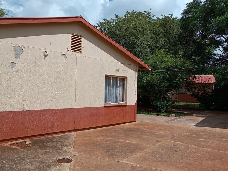 Rear exterior view of the property featuring a concrete driveway, gable roofline, and visible wear to the exterior wall paint and paving surfaces.