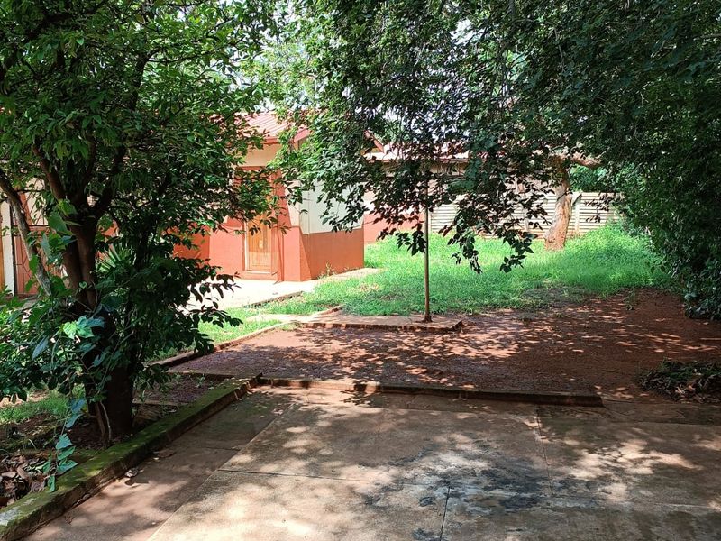 A rear garden area featuring a concrete patio space, mature trees, and a lawn, offering potential for outdoor landscaping and improvement.