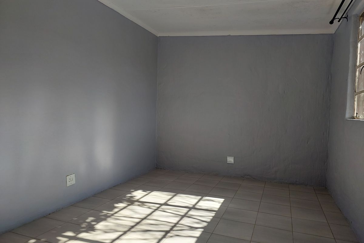 An empty bedroom featuring neutral grey walls, tiled flooring, and natural light streaming through a window with security bars.