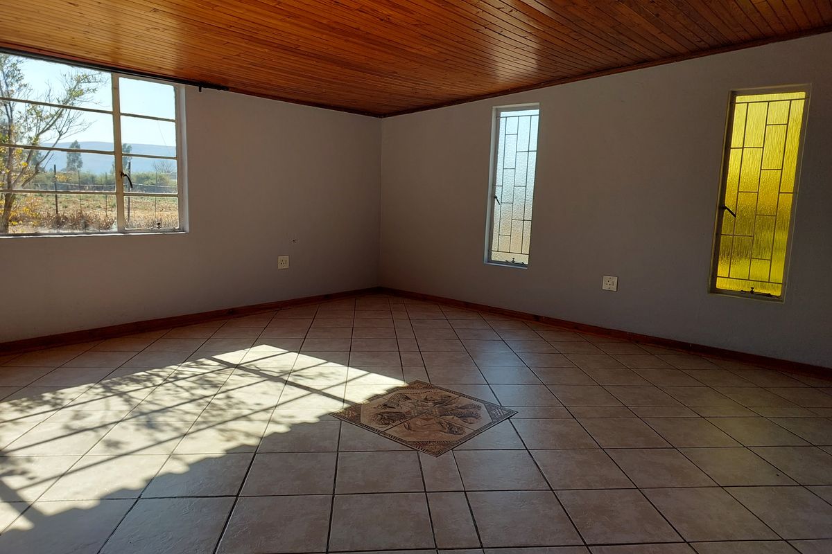 An empty living room featuring ceramic floor tiles with a decorative inlay and a timber tongue and groove ceiling.