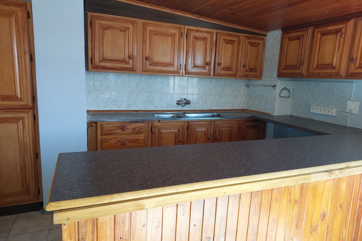 A dated kitchen featuring extensive wooden cabinetry, a breakfast bar, and a double bowl sink with tiled backsplash and timber ceiling.