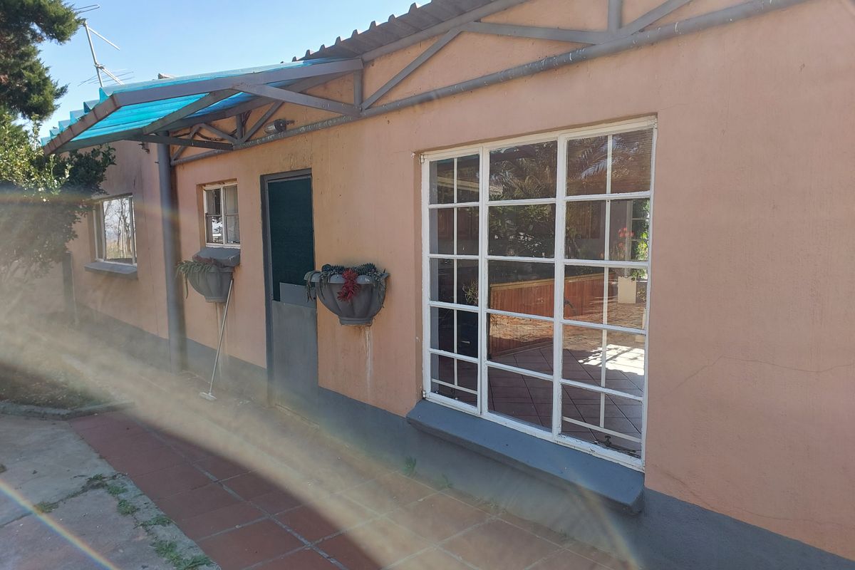 Rear exterior view of the property featuring a tiled patio area, steel-framed windows, and a covered awning structure.