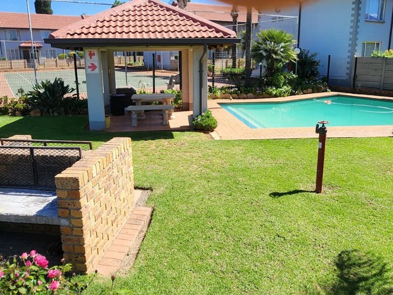 Communal outdoor area featuring a swimming pool, a brick built-in braai, and a covered gazebo, set within a landscaped garden environment.
