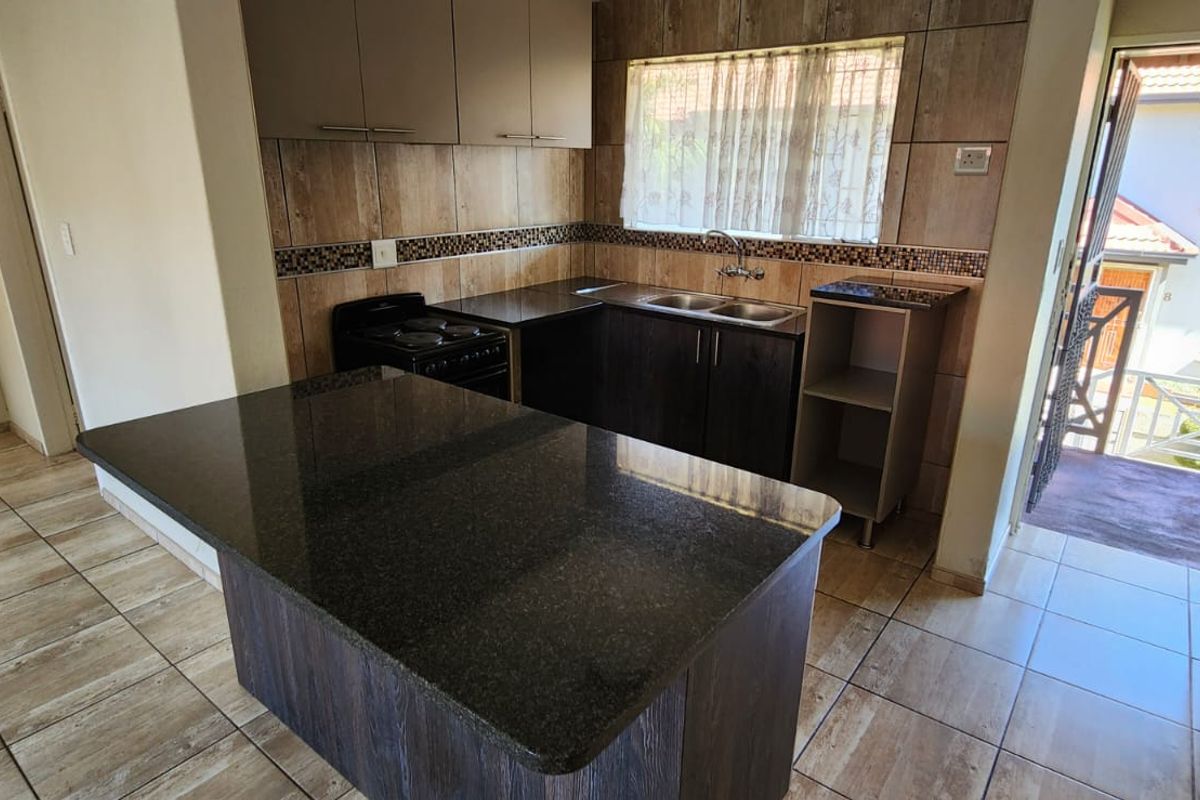 A functional kitchen featuring dark cabinetry, granite countertops, a double basin sink, and tiled flooring, with direct access to an outdoor area.