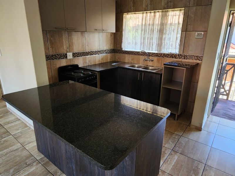 A functional kitchen featuring dark cabinetry, granite countertops, a double basin sink, and tiled flooring, with direct access to an outdoor area.