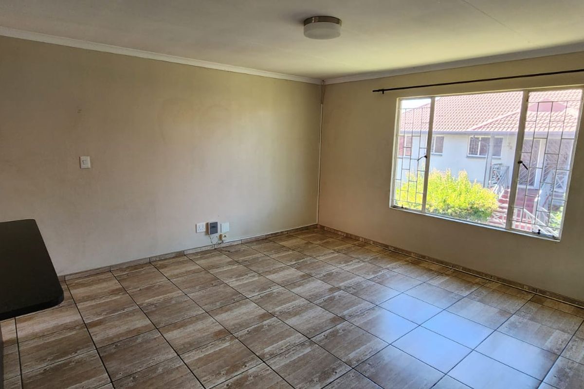 An empty living room featuring tiled flooring, a large window with security bars, and neutral wall finishes, ready for personalization.