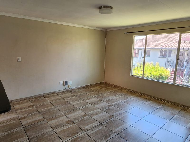 An empty living room featuring tiled flooring, a large window with security bars, and neutral wall finishes, ready for personalization.