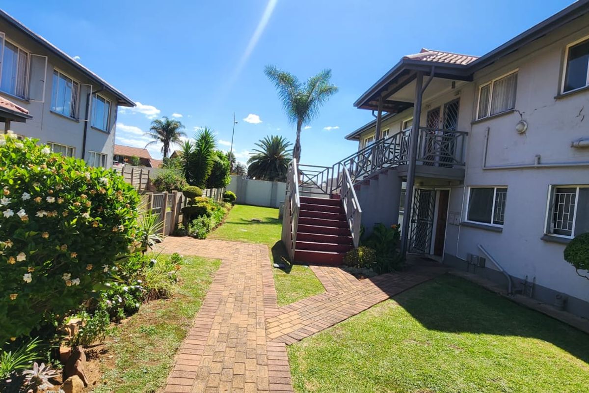 A view of the rear exterior of the townhouse complex, featuring a landscaped garden, brick paved pathways, and an external staircase leading to upper units.