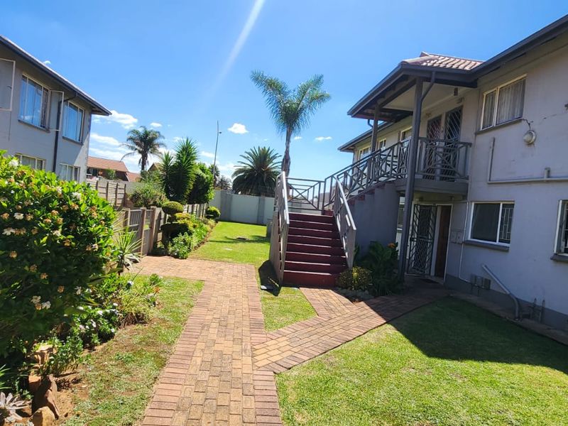 A view of the rear exterior of the townhouse complex, featuring a landscaped garden, brick paved pathways, and an external staircase leading to upper units.