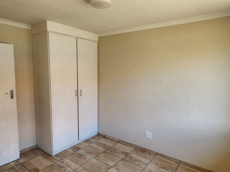 A vacant bedroom featuring tiled flooring, a built-in wardrobe, and a window with security bars.