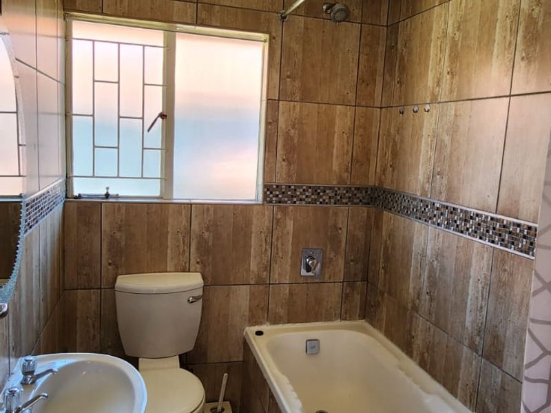 A compact bathroom featuring a bathtub, pedestal basin, and toilet with full-height wood-look wall tiling and a textured ceiling finish.