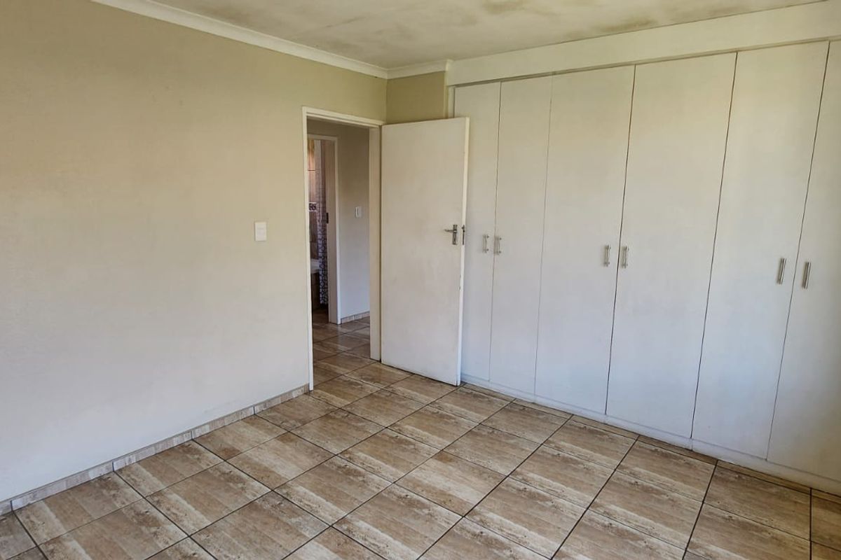 An empty bedroom featuring tiled flooring and built-in cupboards, showing signs of wear on the walls and ceiling.