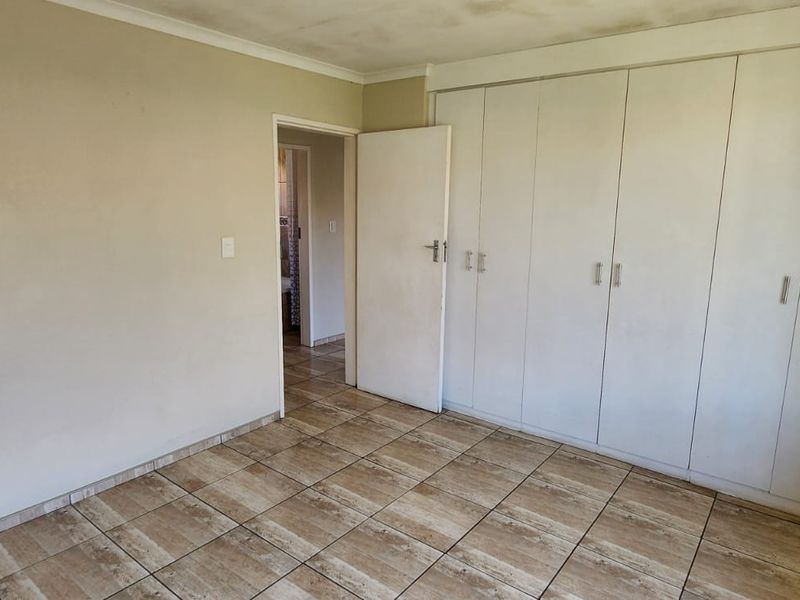 An empty bedroom featuring tiled flooring and built-in cupboards, showing signs of wear on the walls and ceiling.